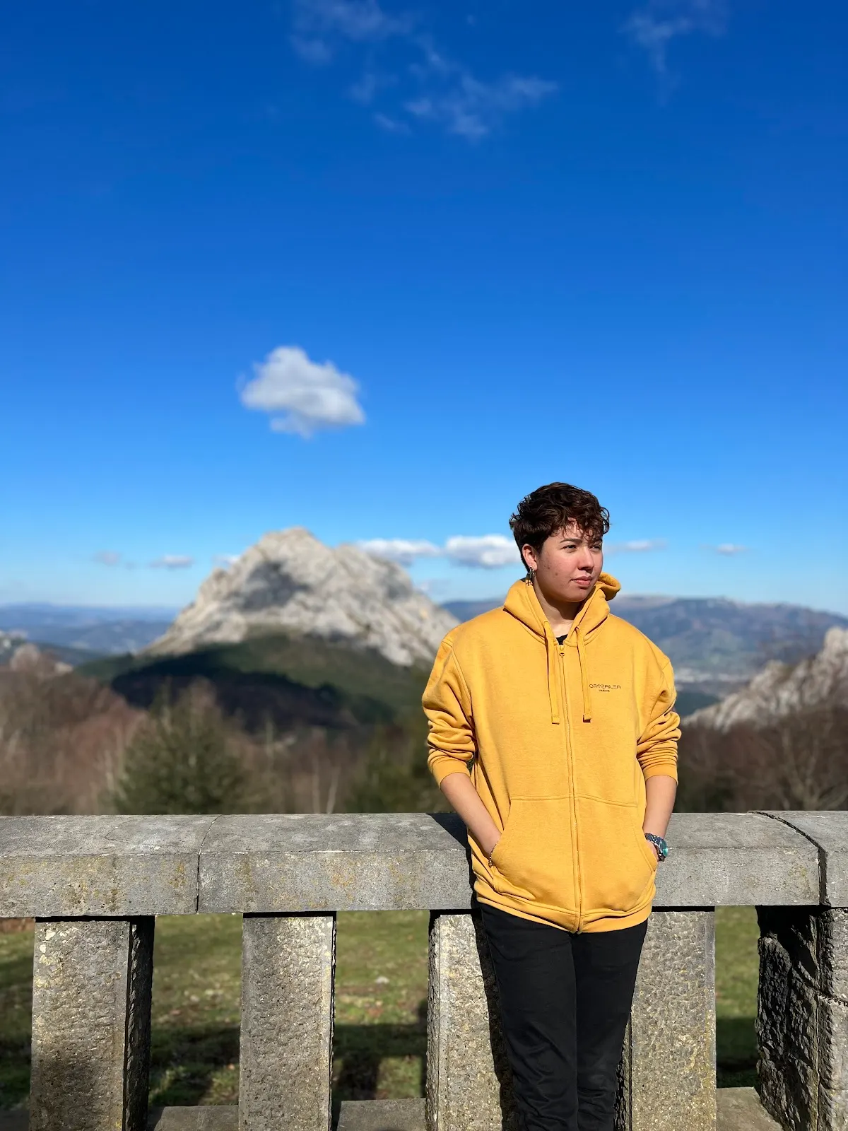 Ana Dos Santos con una sudadera amarilla frente a un paisaje de montaña.