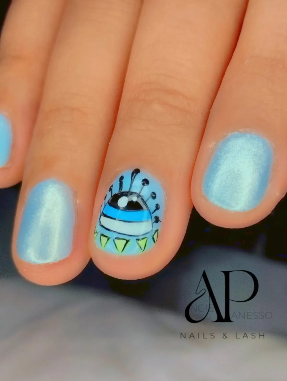 Uñas cortas esmaltadas en azul con un diseño ilustrado en una uña.