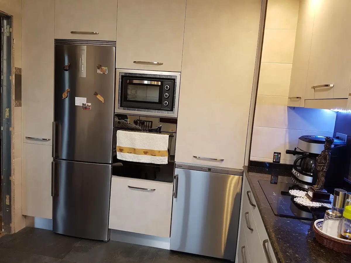 Cocina equipada con muebles claros, electrodomésticos y encimera oscura.