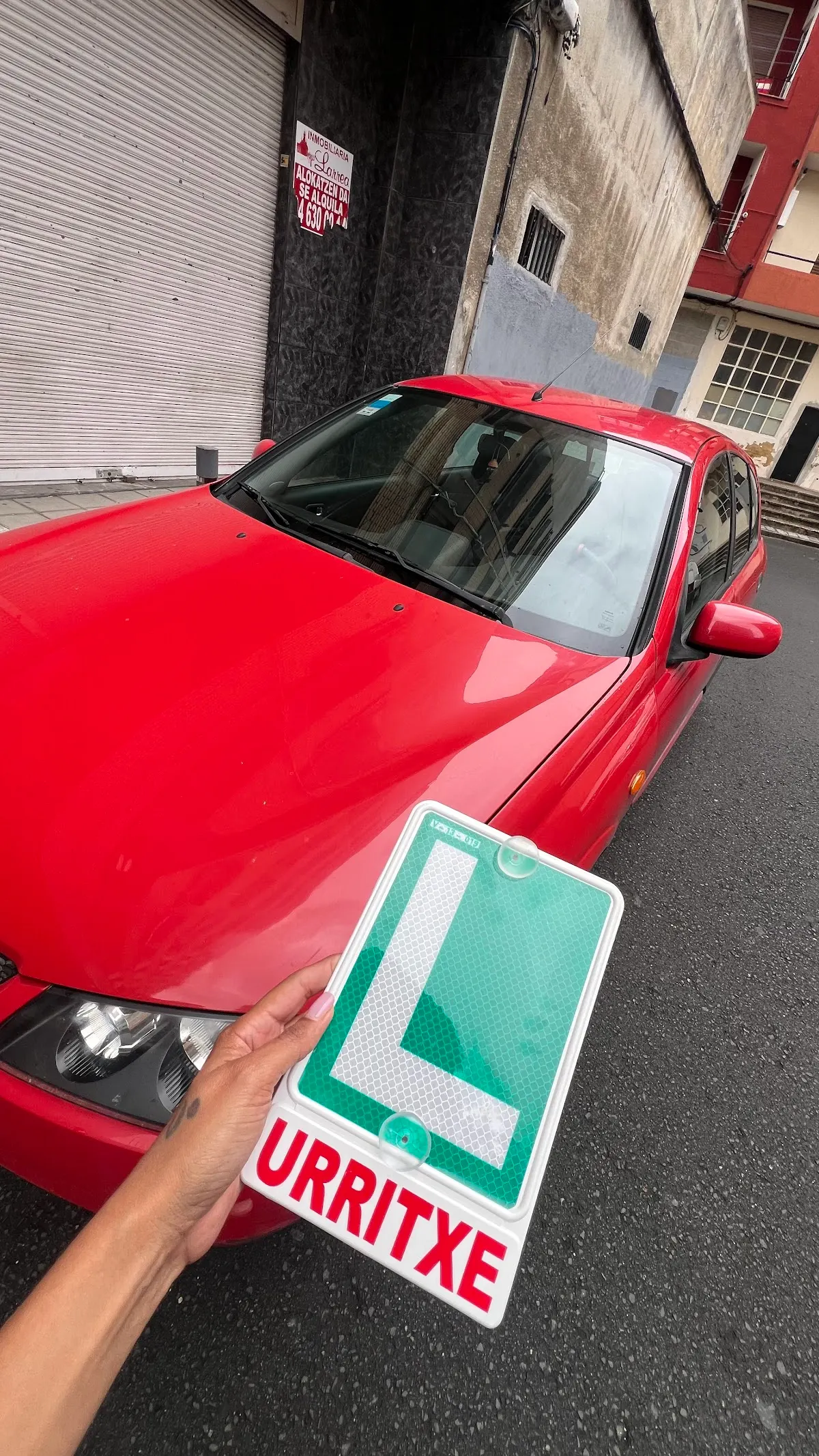 Distintivo de Autoescuela Urritxe junto a un coche rojo