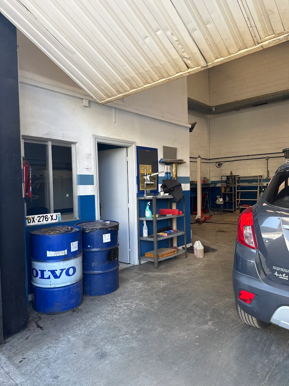 Interior del taller Balen auto, con herramientas y bidones de aceite junto a un vehículo.