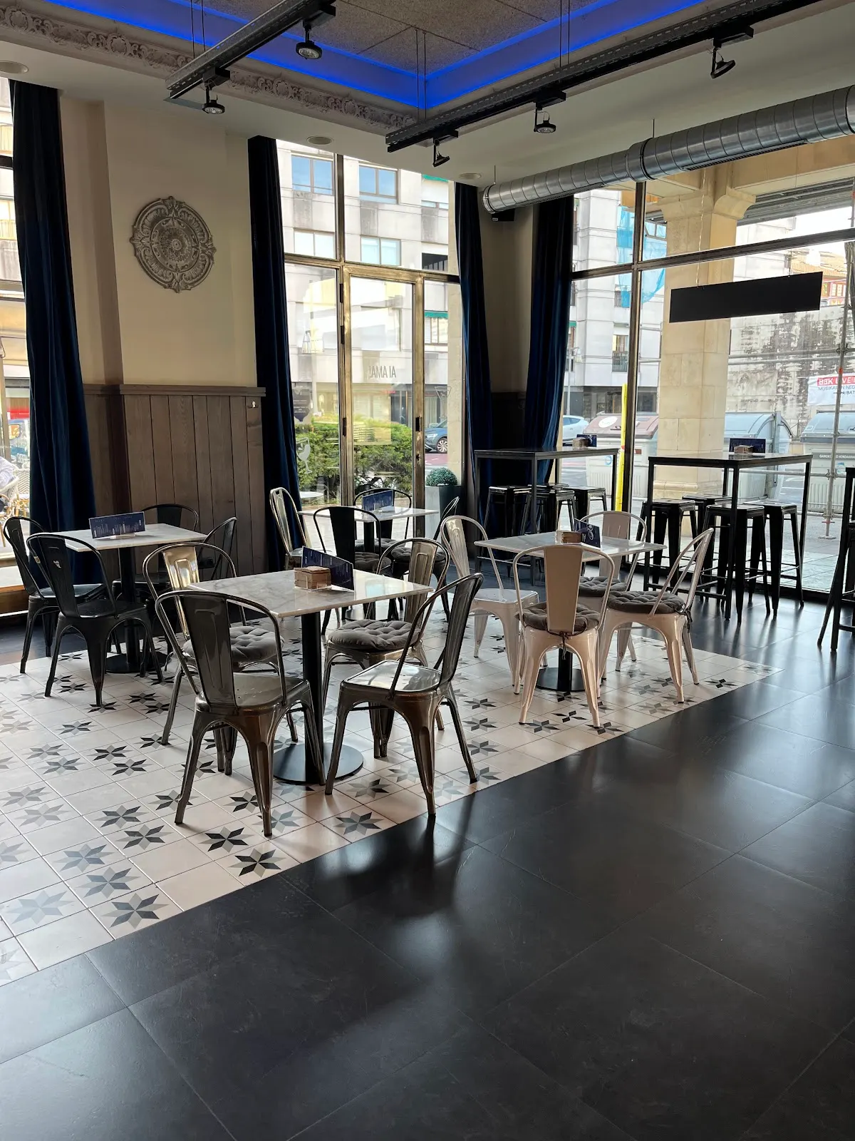 Interior de Bar Ai Ama, con mesas y sillas junto a grandes ventanales.