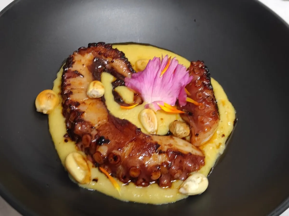 Pulpo servido sobre una crema, con frutos secos y decoración floral.