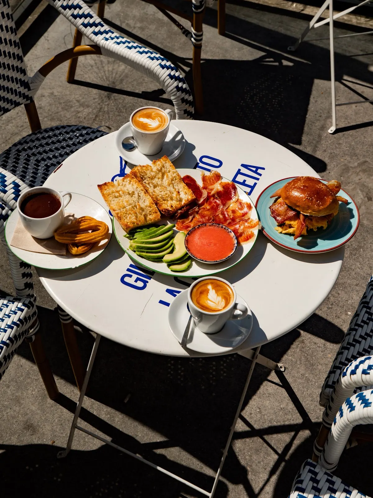 Desayuno en una mesa de terraza con cafés, tostadas y otros platos.