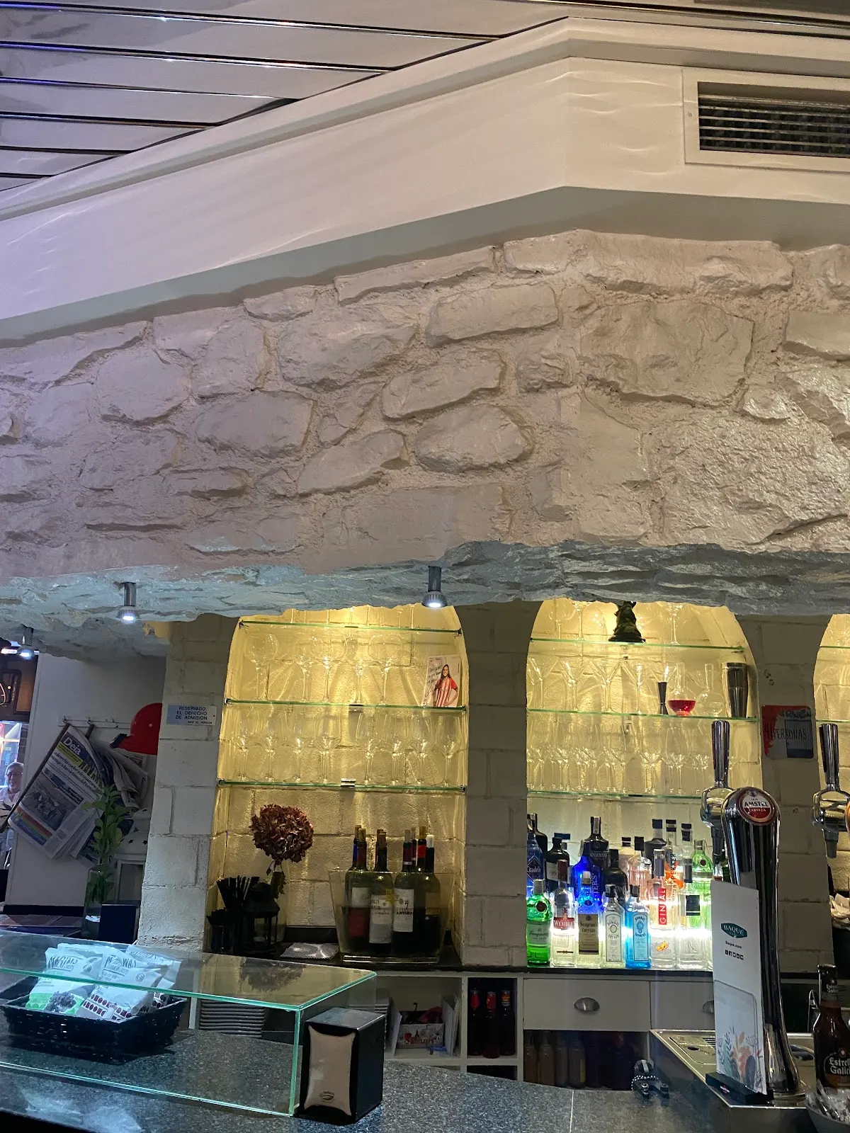 Barra de Bar El Rincón, con botellas y vitrinas iluminadas.