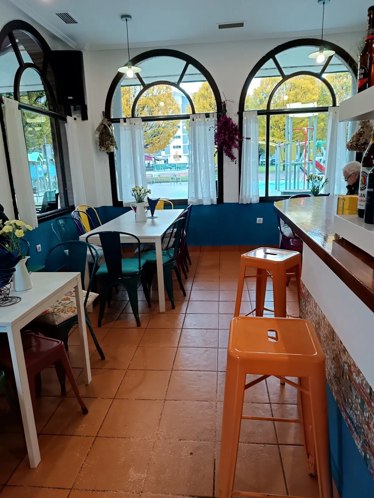 Interior de Bar Goxoa, con mesas junto a ventanas arqueadas y una barra.