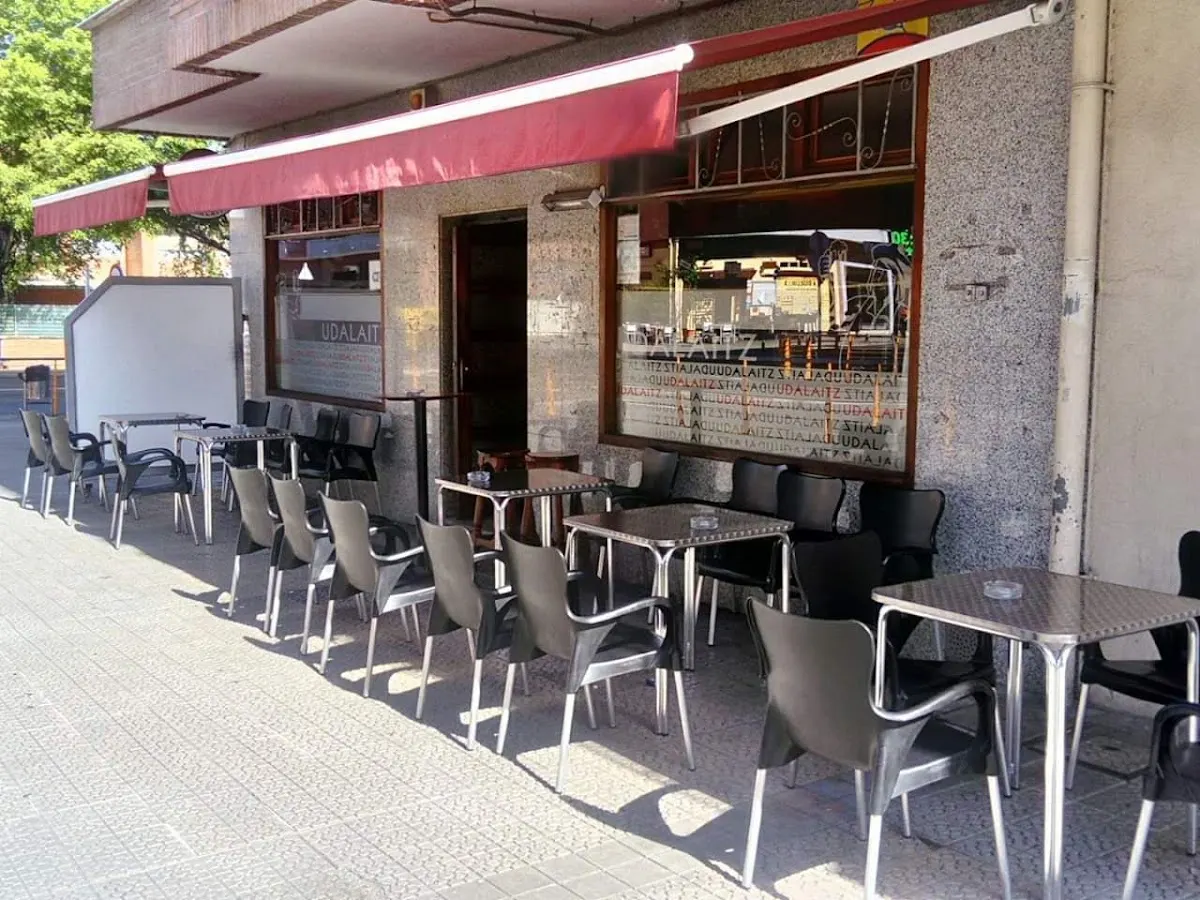 Terraza exterior de Bar Udalaitz con mesas y sillas bajo un toldo rojo