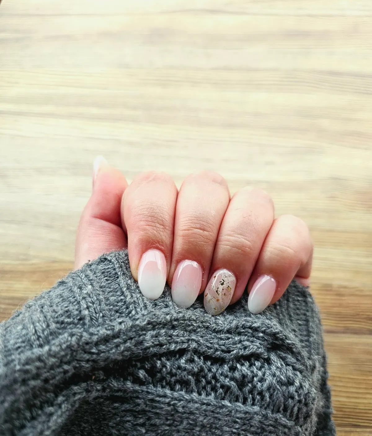 Manicura de uñas claras con detalle decorativo sobre una prenda de punto gris.