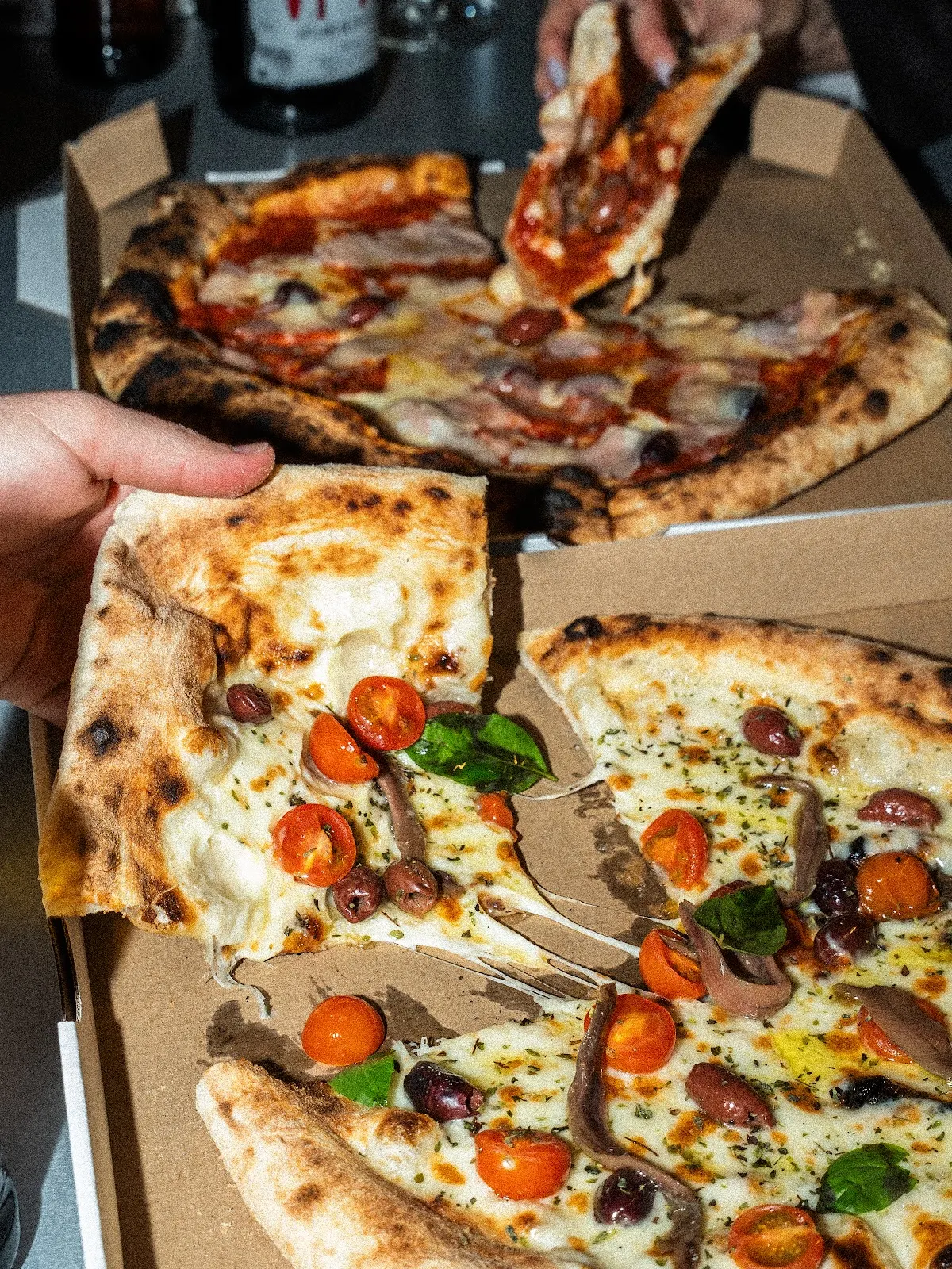 Varias porciones de pizza con queso, verduras y otros ingredientes en cajas de cartón.