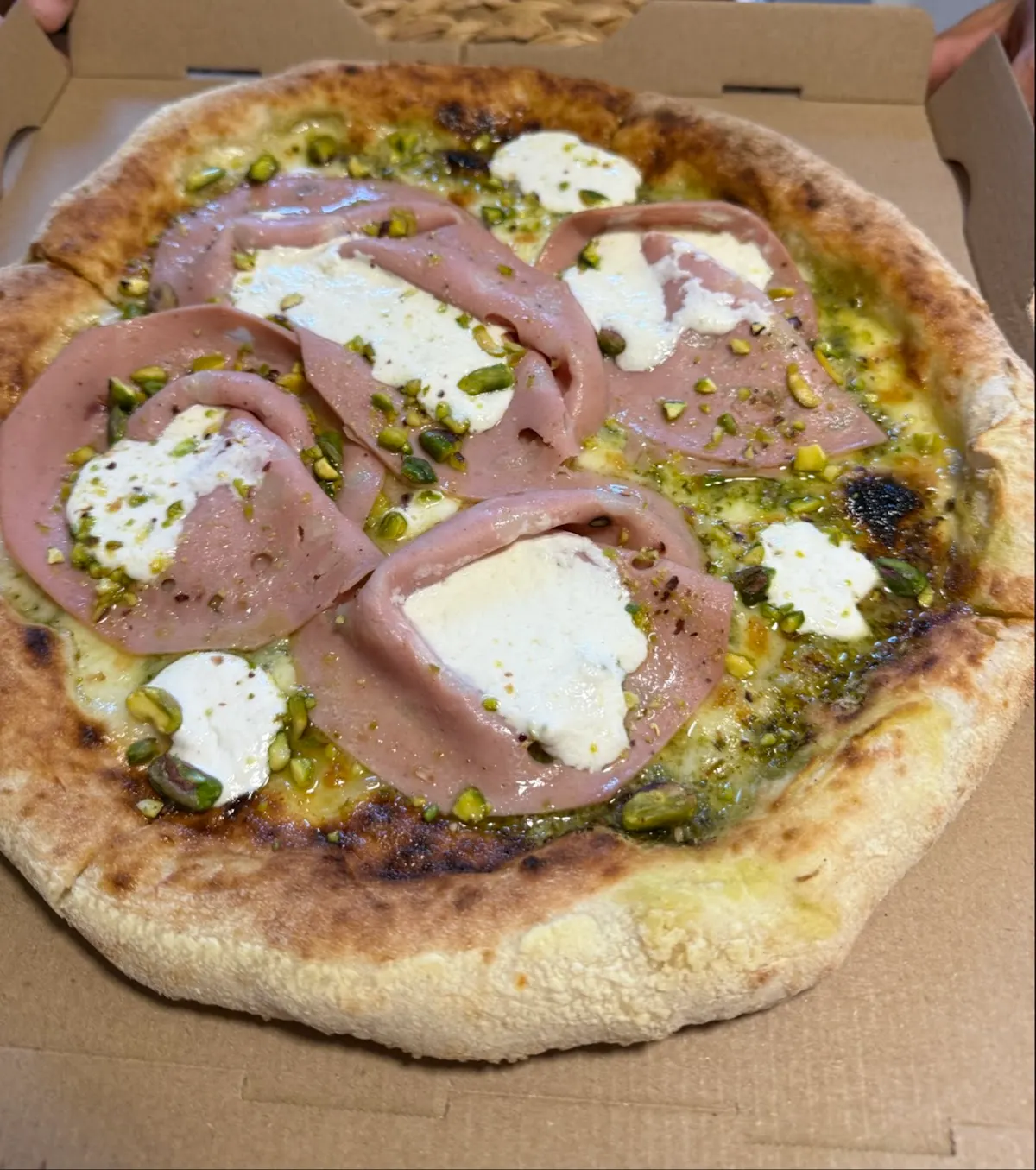 Pizza con mozzarella, mortadela y pistachos en una caja para llevar.