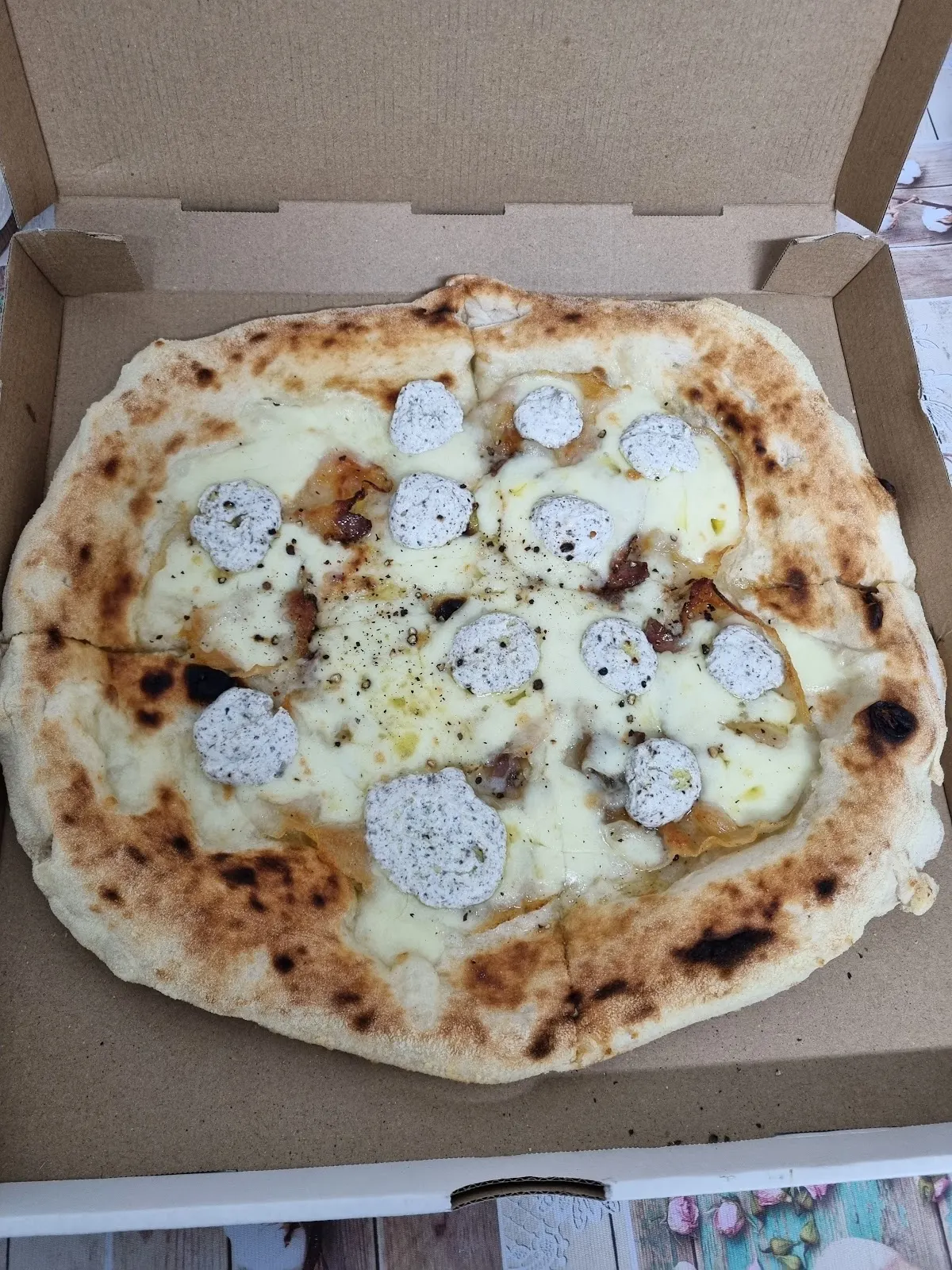 Pizza de queso con porciones de ricotta en una caja de cartón.