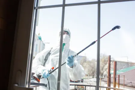 Profesional con equipo de protección limpia una ventana desde el exterior.