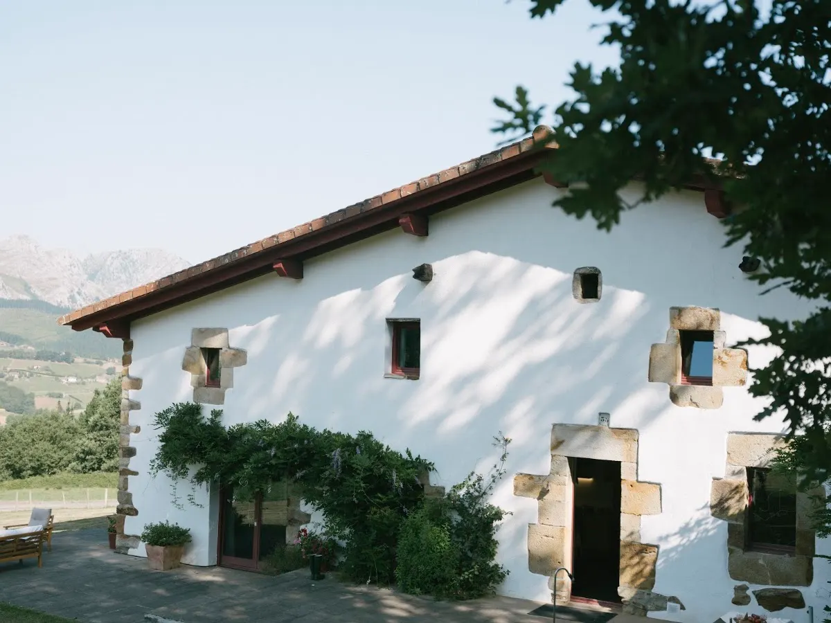 Fachada de Casa Goikomaia, un caserío blanco rodeado de vegetación