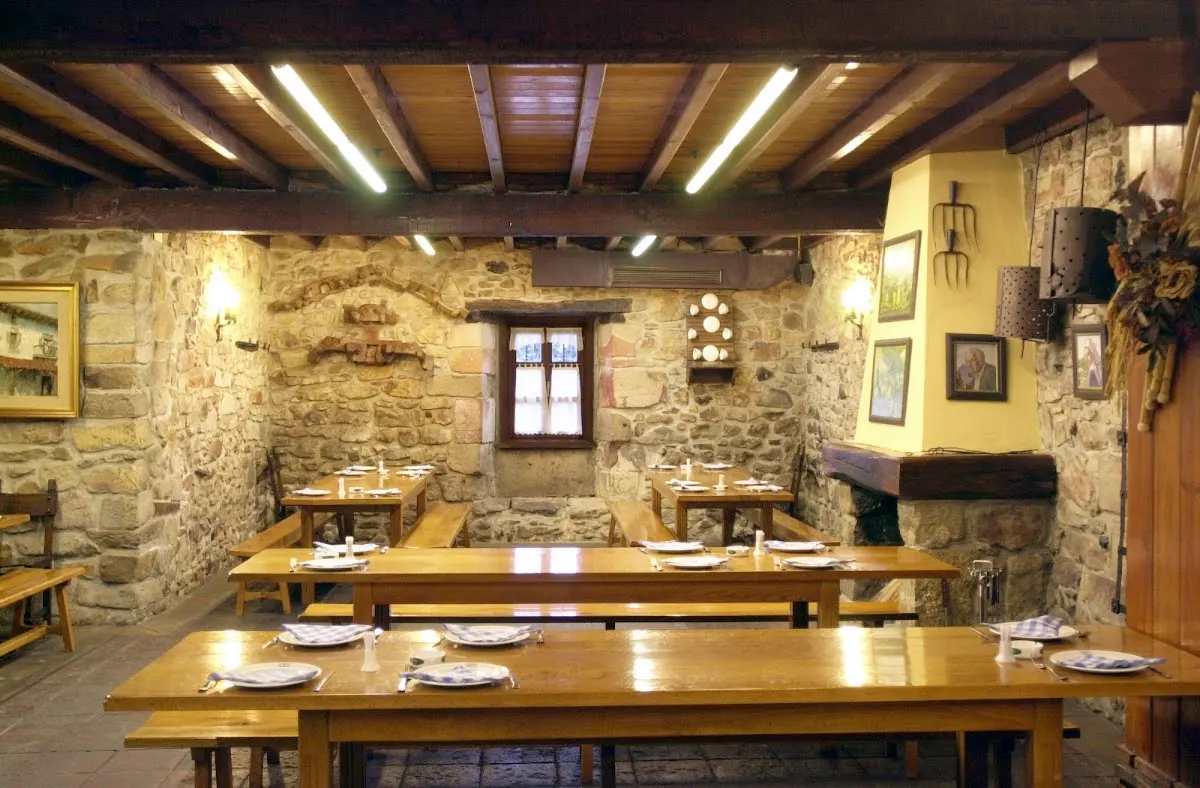 Comedor de piedra de Cervecera Sidrería Ibarra Sagardotegia, con mesas de madera y vigas vistas.