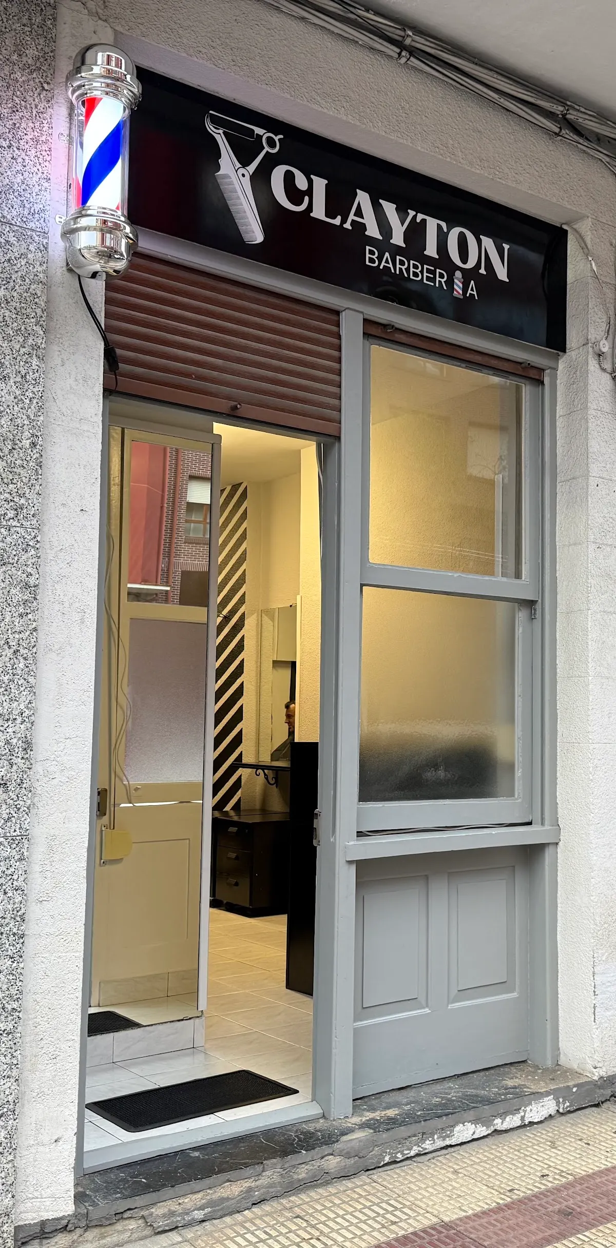 Entrada de Clayton Barbería, con el rótulo y el poste de barbero junto a la puerta.