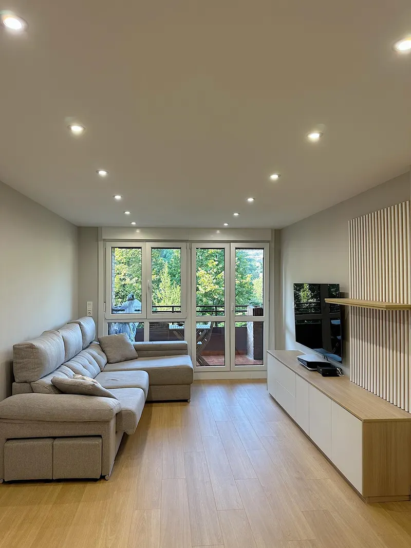 Salón reformado con sofá, ventanas amplias y suelo de madera