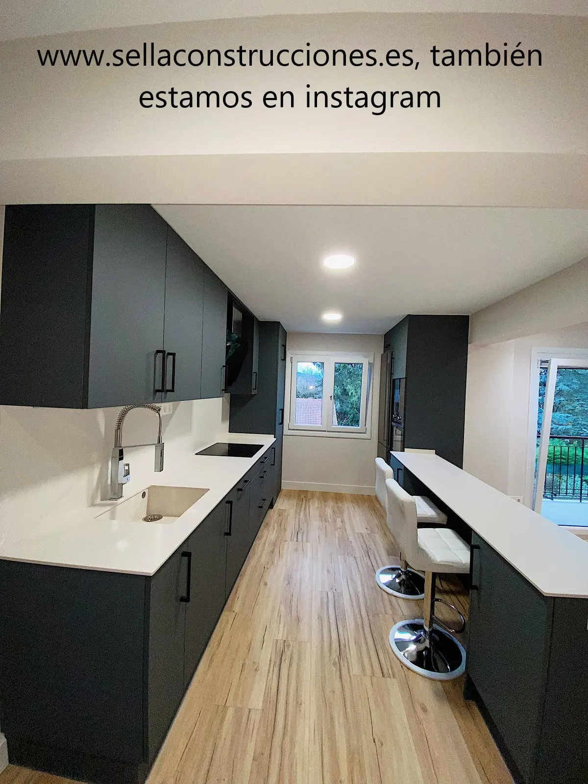 Cocina reformada con muebles oscuros e isla con barra por Construcciones Sella
