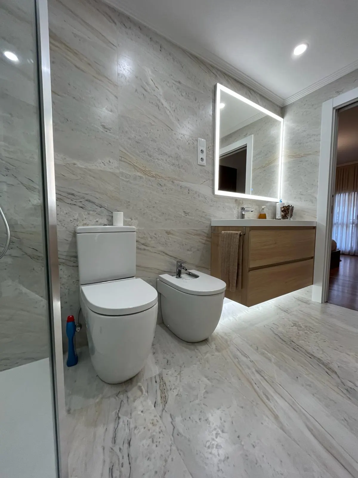 Cuarto de baño reformado con revestimiento de mármol, ducha y sanitarios.