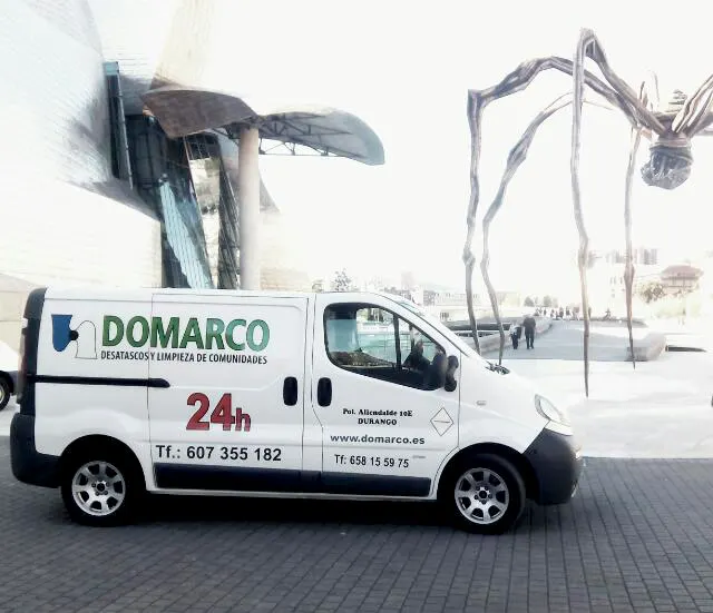 Furgoneta de Desatascos Domarco en una plaza, con el teléfono y la atención 24 horas visibles.