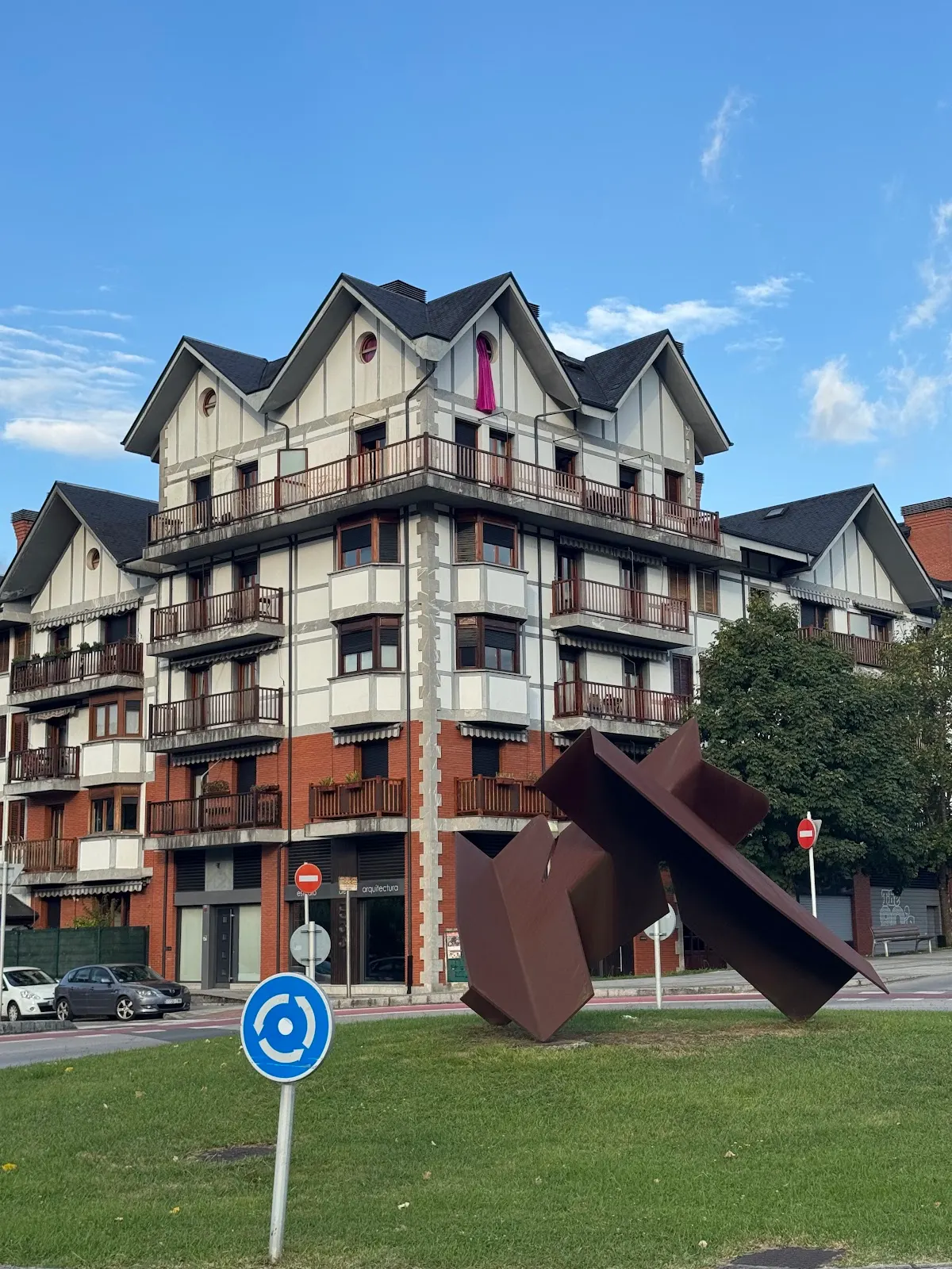 Edificio de viviendas en una esquina de Durango, junto a una escultura abstracta en una rotonda.