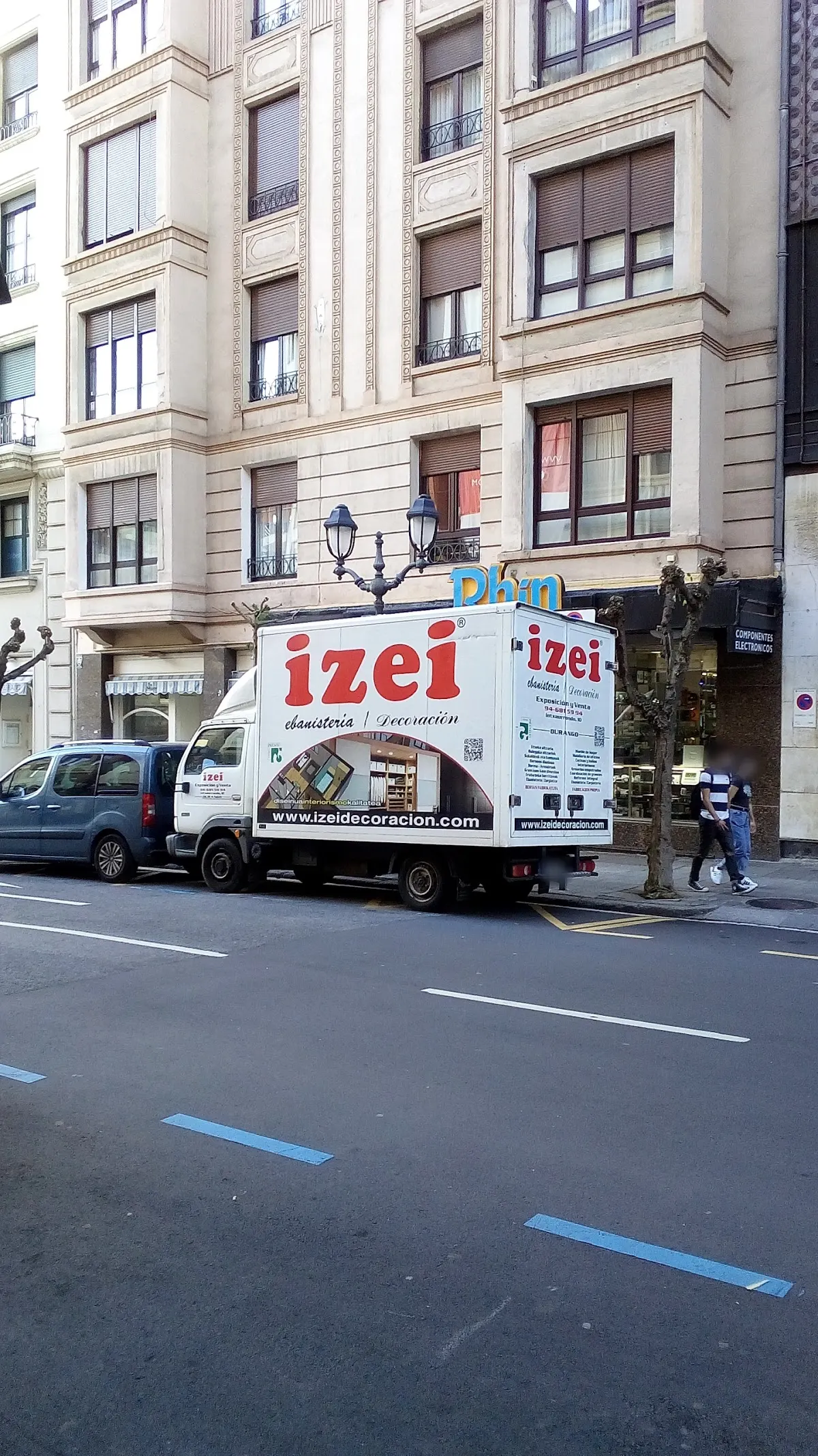 Camión rotulado de Ebanistería Izei aparcado frente a un edificio en una calle de Durango.