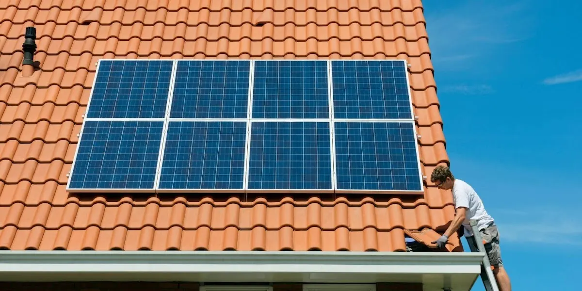 Técnico trabajando junto a paneles solares en el tejado de una vivienda.