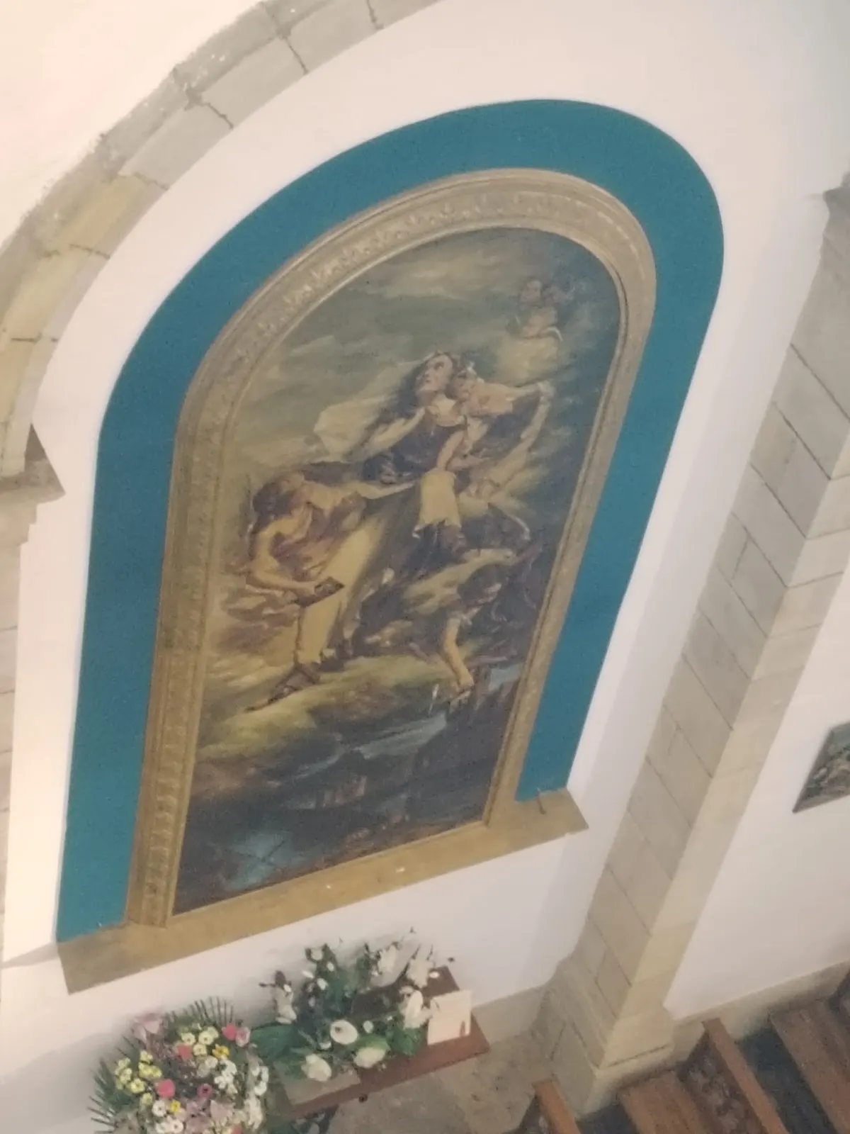 Pintura religiosa en una bóveda, sobre un altar con flores.