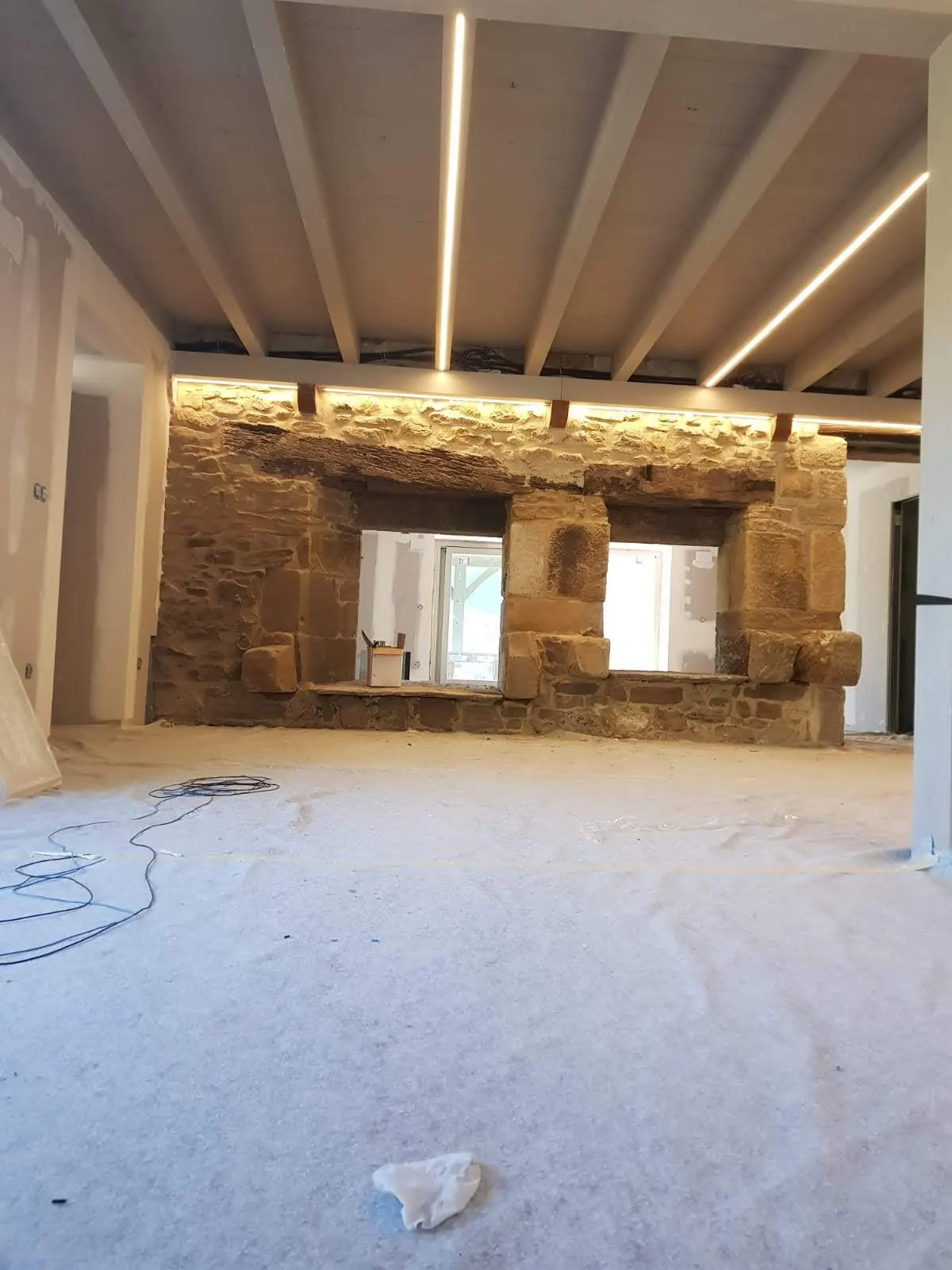 Estancia en obras con muros de piedra y líneas de iluminación en el techo