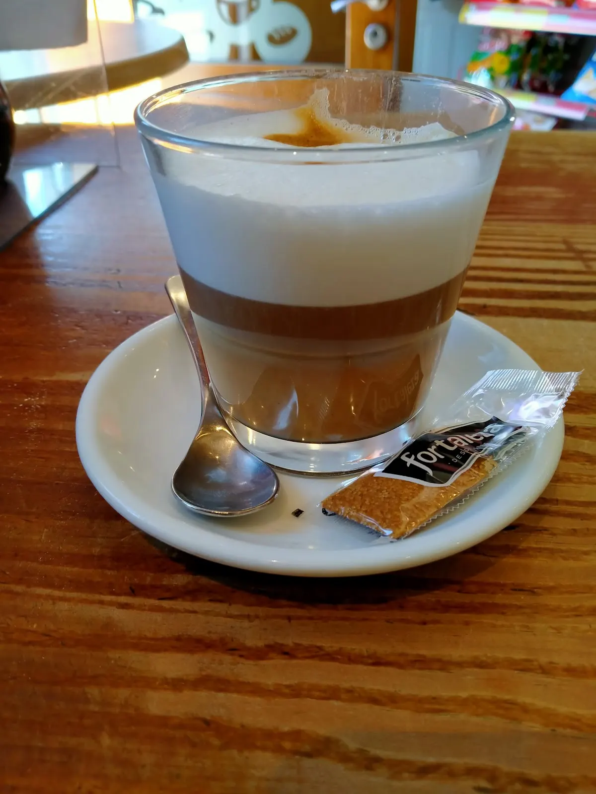 Café con leche servido en una taza de cristal sobre una mesa de madera