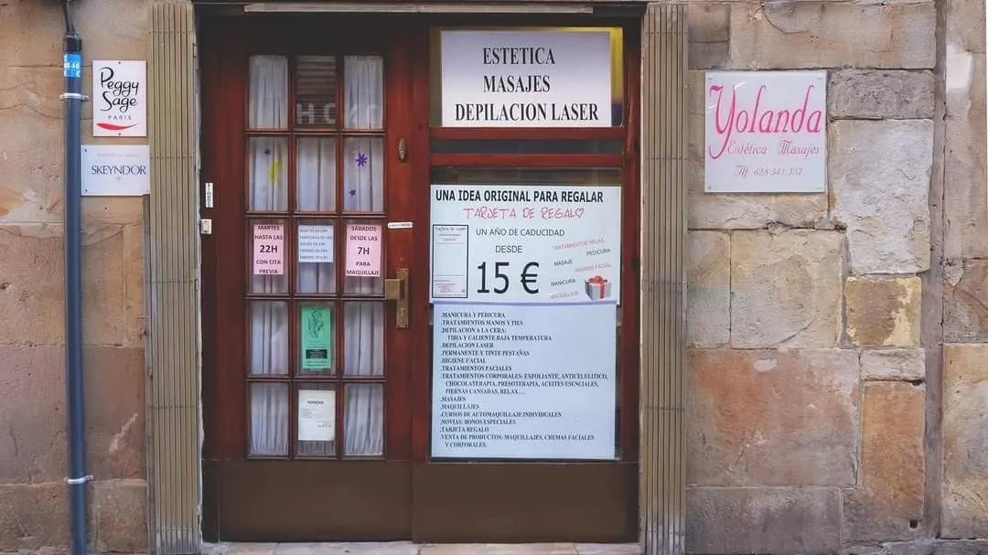 Entrada de Estética Yolanda en una fachada de piedra, con carteles de estética, masajes y depilación láser.