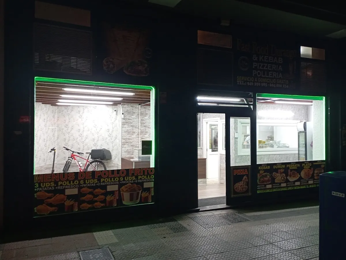 Fachada iluminada de FAST FOOD DURANGO por la noche, con el acceso y los escaparates del local.