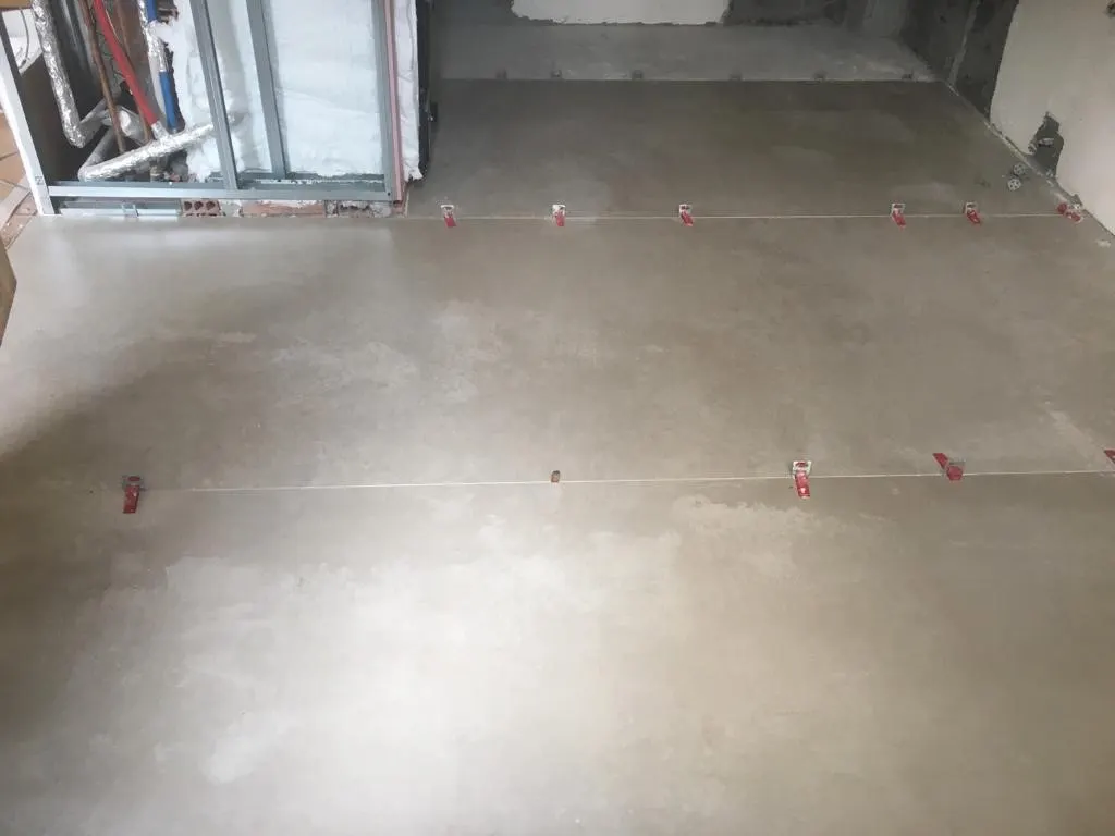 Suelo de una estancia en obra con piezas colocadas y niveladores rojos