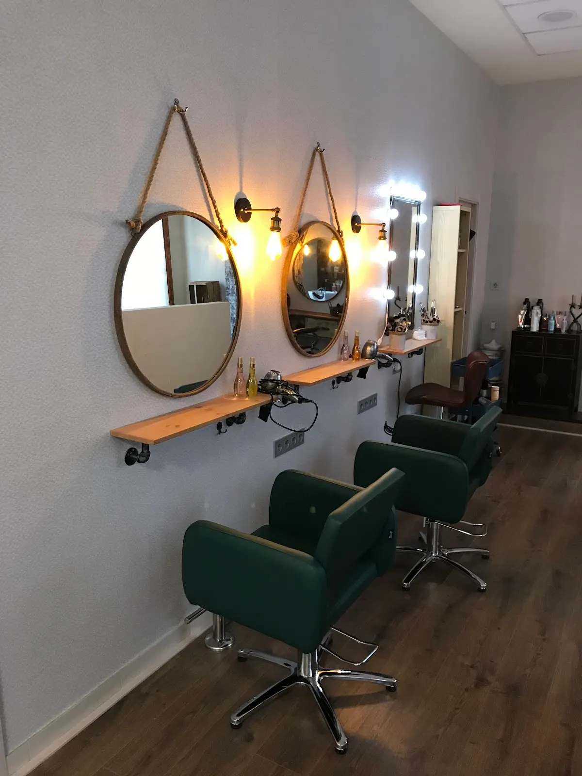 Puestos de peluquería con espejos y sillones verdes en Hemai