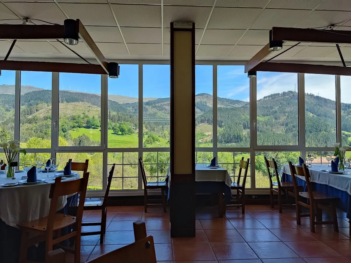Comedor de Herriko Jatetxea Garai con mesas junto a grandes ventanales y vistas a las montañas