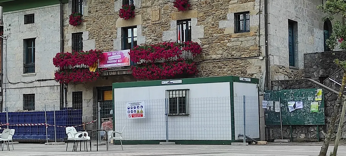 Fachada de Herriko Taberna Mañaria en una plaza del municipio, con flores en los balcones y terraza exterior.