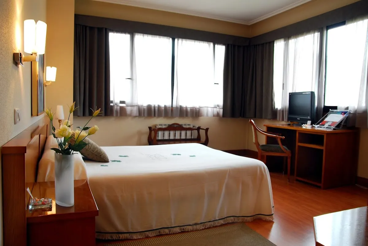 Habitación del Hotel Elorrio con cama, escritorio y grandes ventanales.