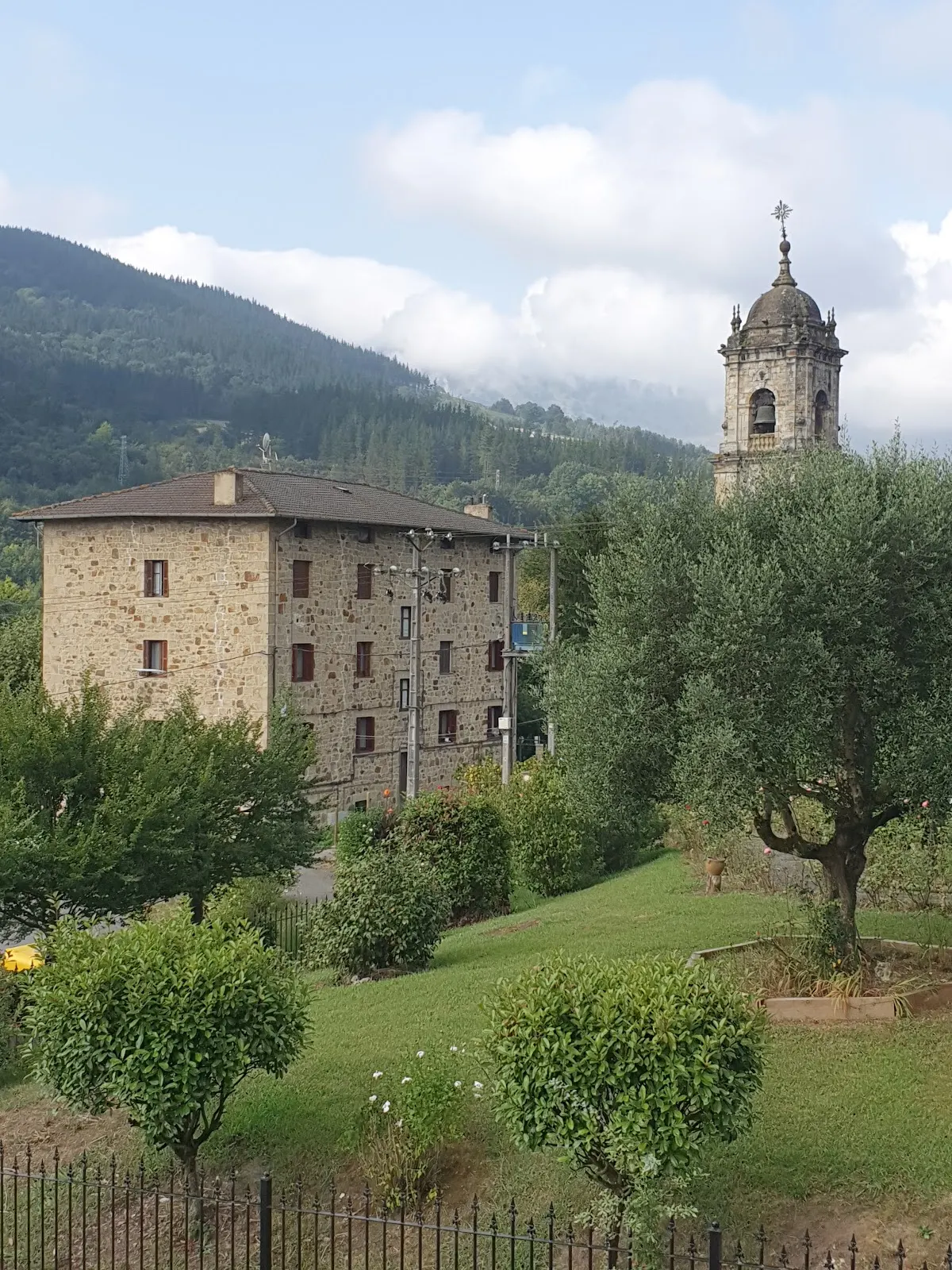 Edificio del Hotel Elorrio entre jardines y montañas, junto a una torre.
