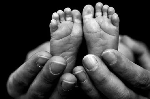 Imagen en blanco y negro de unos pies de bebé sostenidos con las manos.