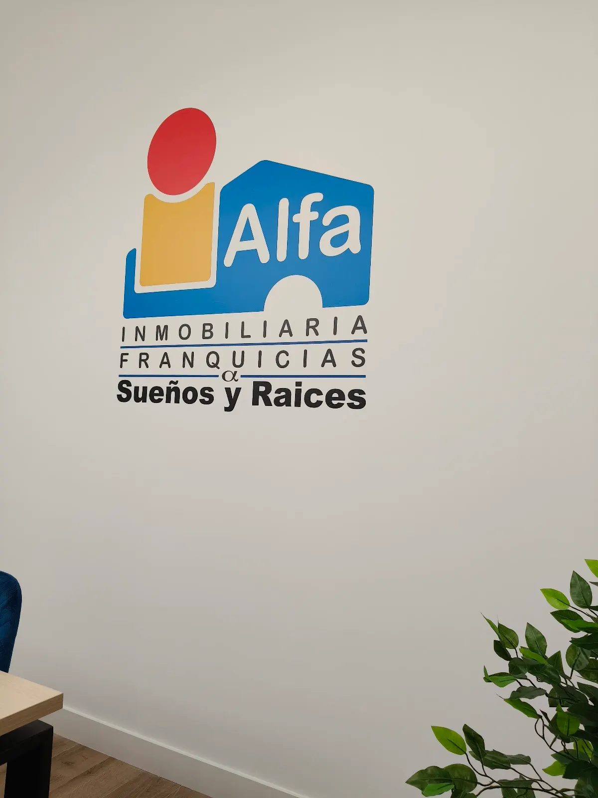 Logotipo de Inmobiliaria Alfa Sueños y Raíces en una pared