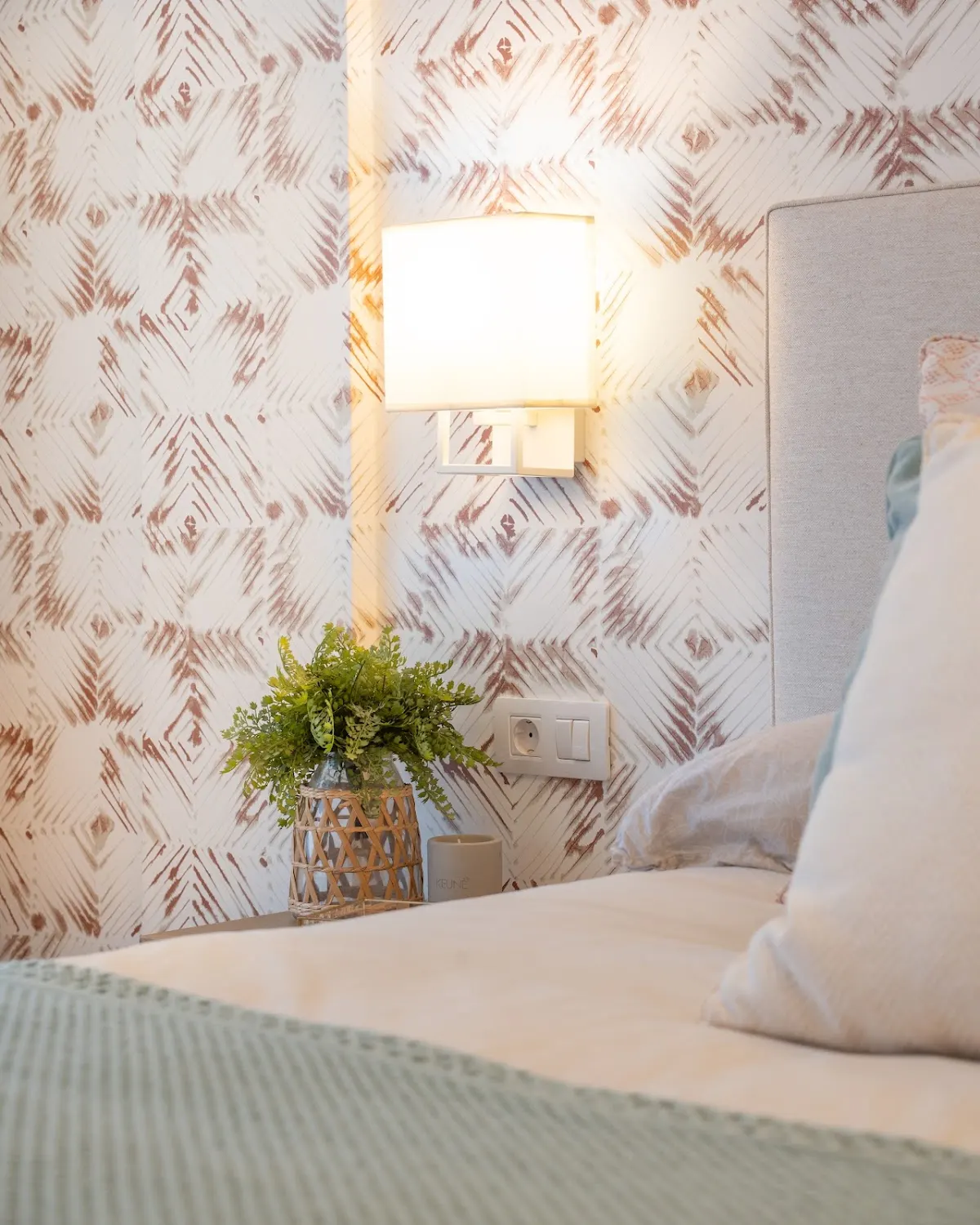 Detalle de dormitorio con papel pintado, lámpara y mesilla, en una imagen de interiores de Alki