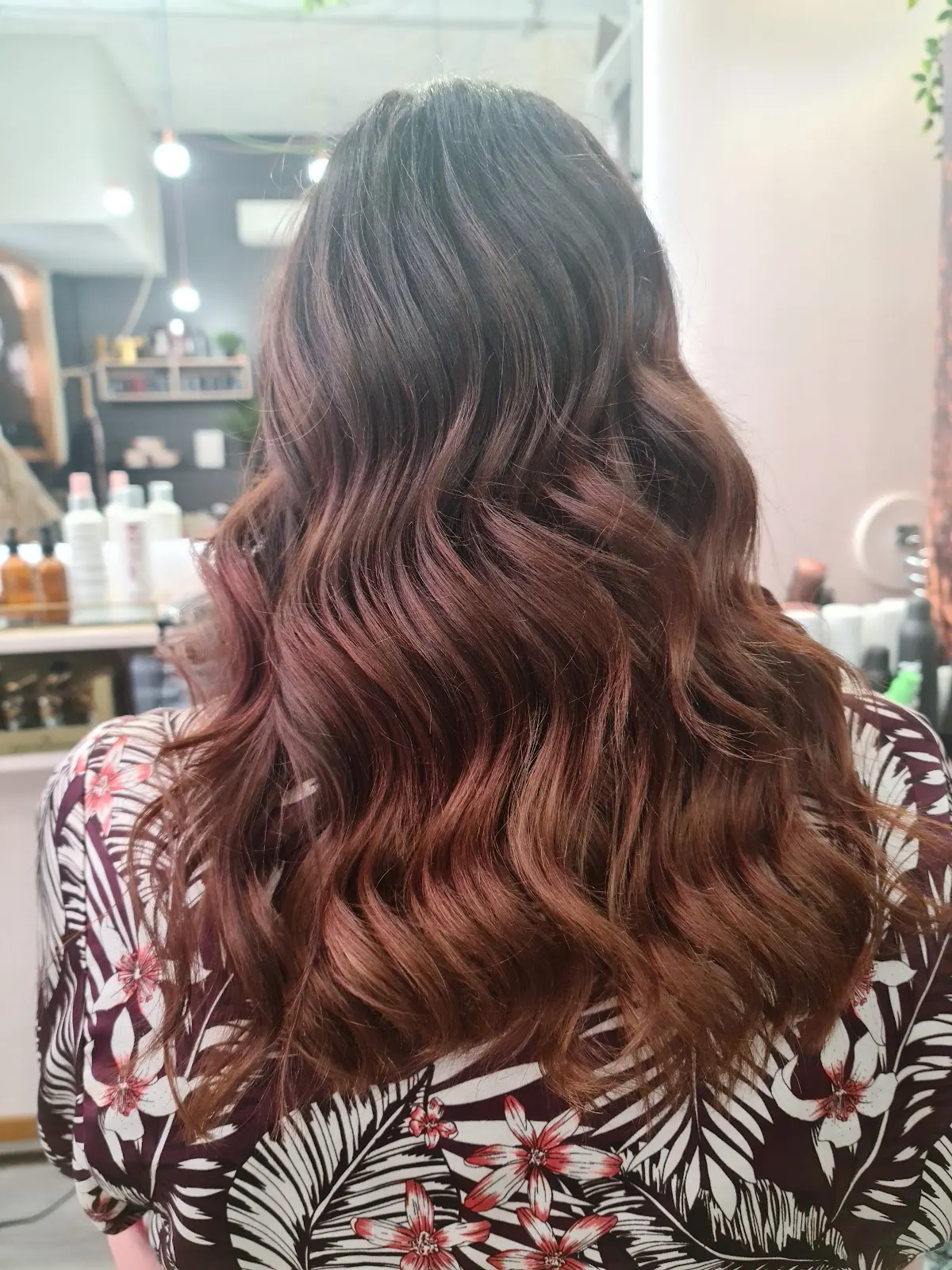 Cabello largo ondulado castaño con reflejos rojizos en el interior de una peluquería.