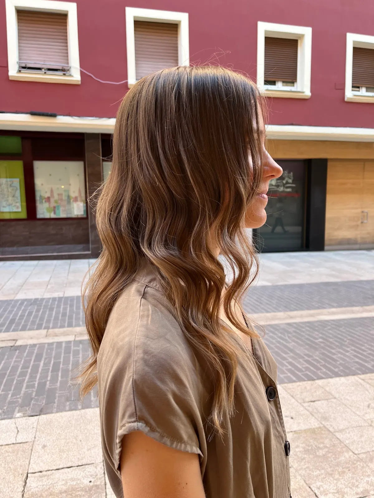 Perfil de una mujer con el cabello largo castaño y ondulado en una calle.