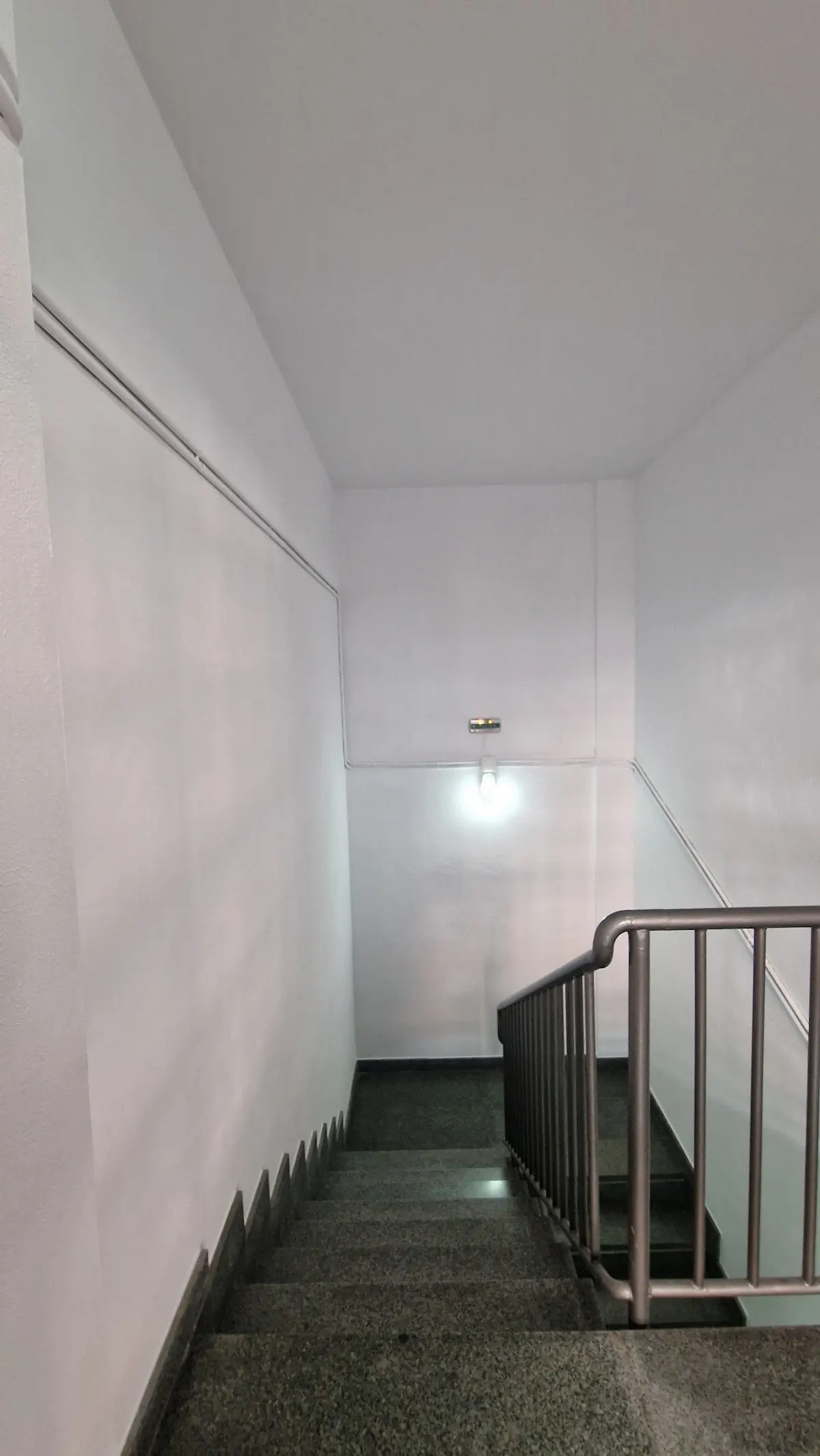 Tramo de escalera comunitaria con paredes blancas y pasamanos metálico, en una imagen de Kadi Pintores