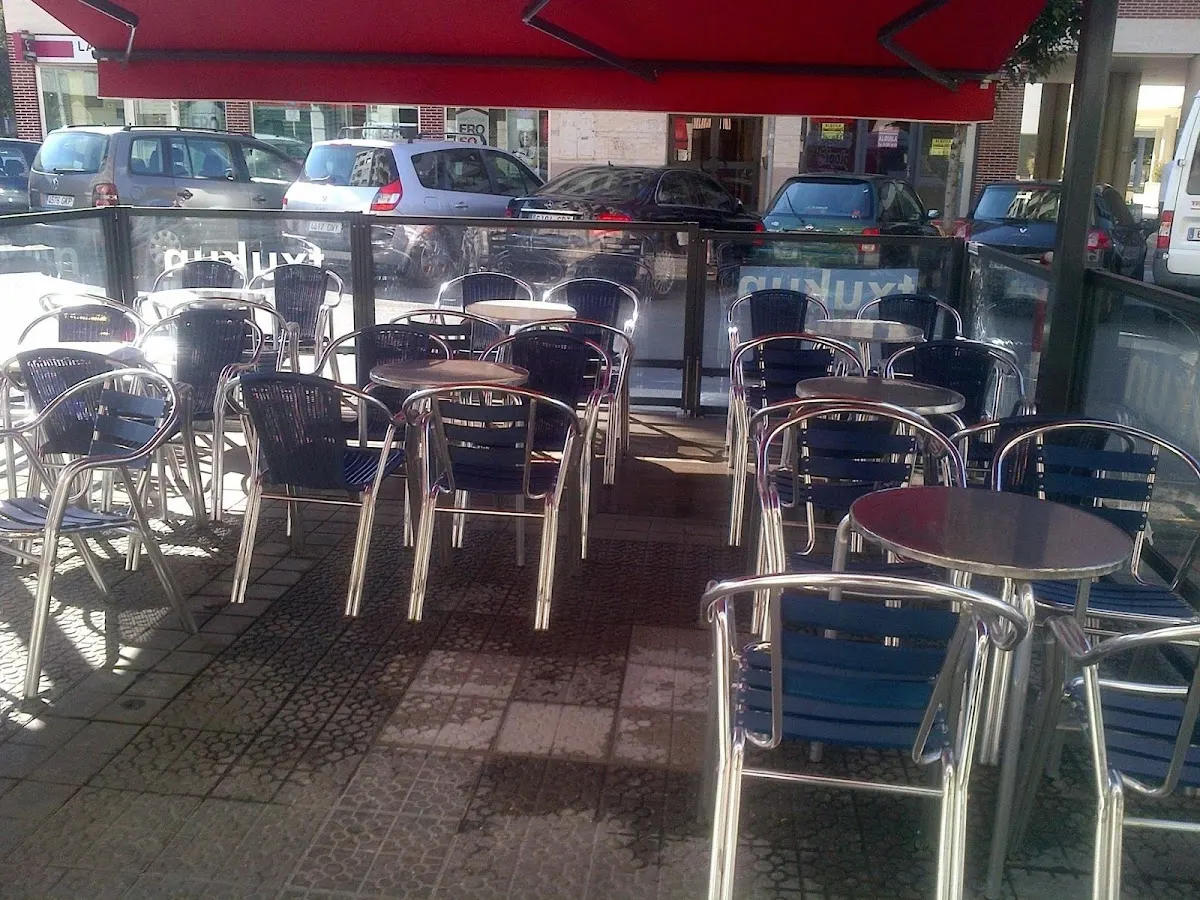 Terraza exterior de Kafeteria Txukun, con mesas y sillas bajo un toldo rojo.