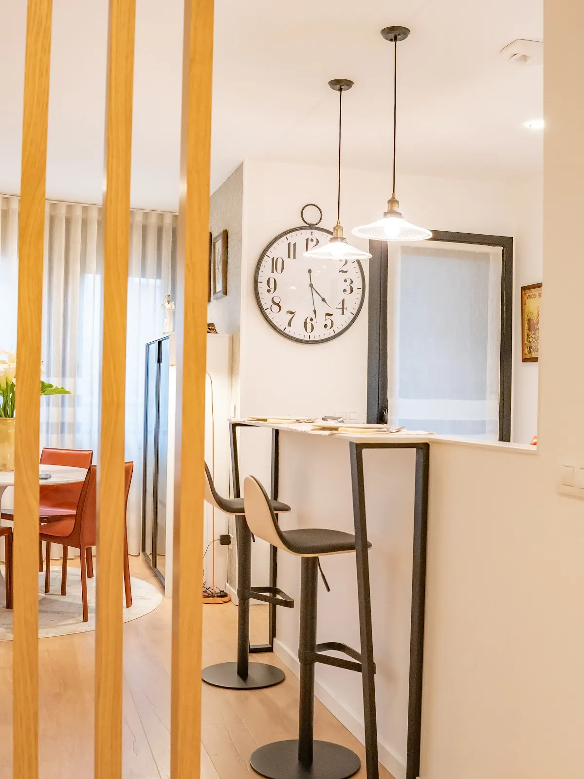 Zona de comedor y barra con taburetes, separada por listones de madera.
