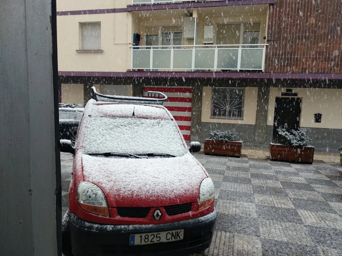 Coche rojo cubierto de nieve frente a un edificio en Berriz