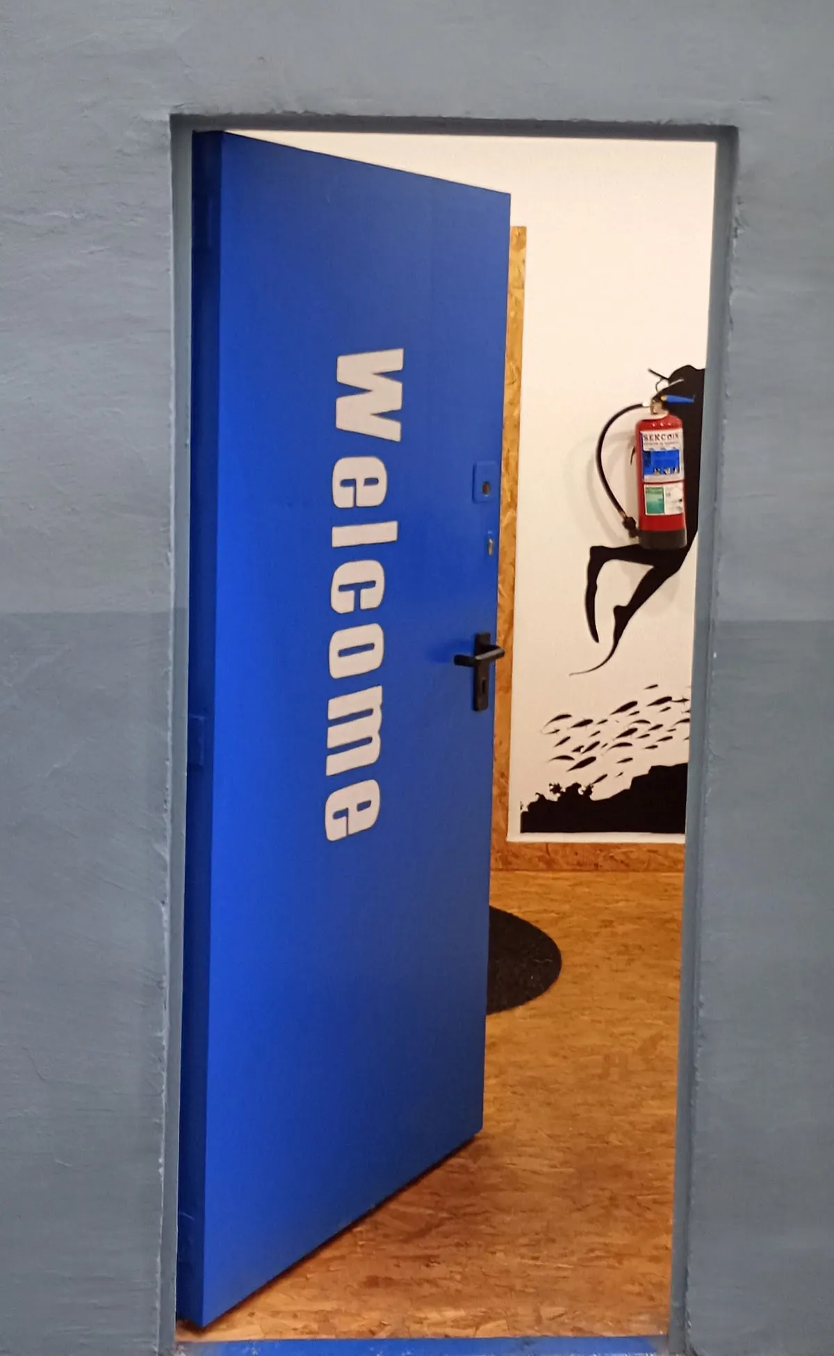 Entrada abierta de Let’s Talk con la puerta azul y el rótulo Welcome.