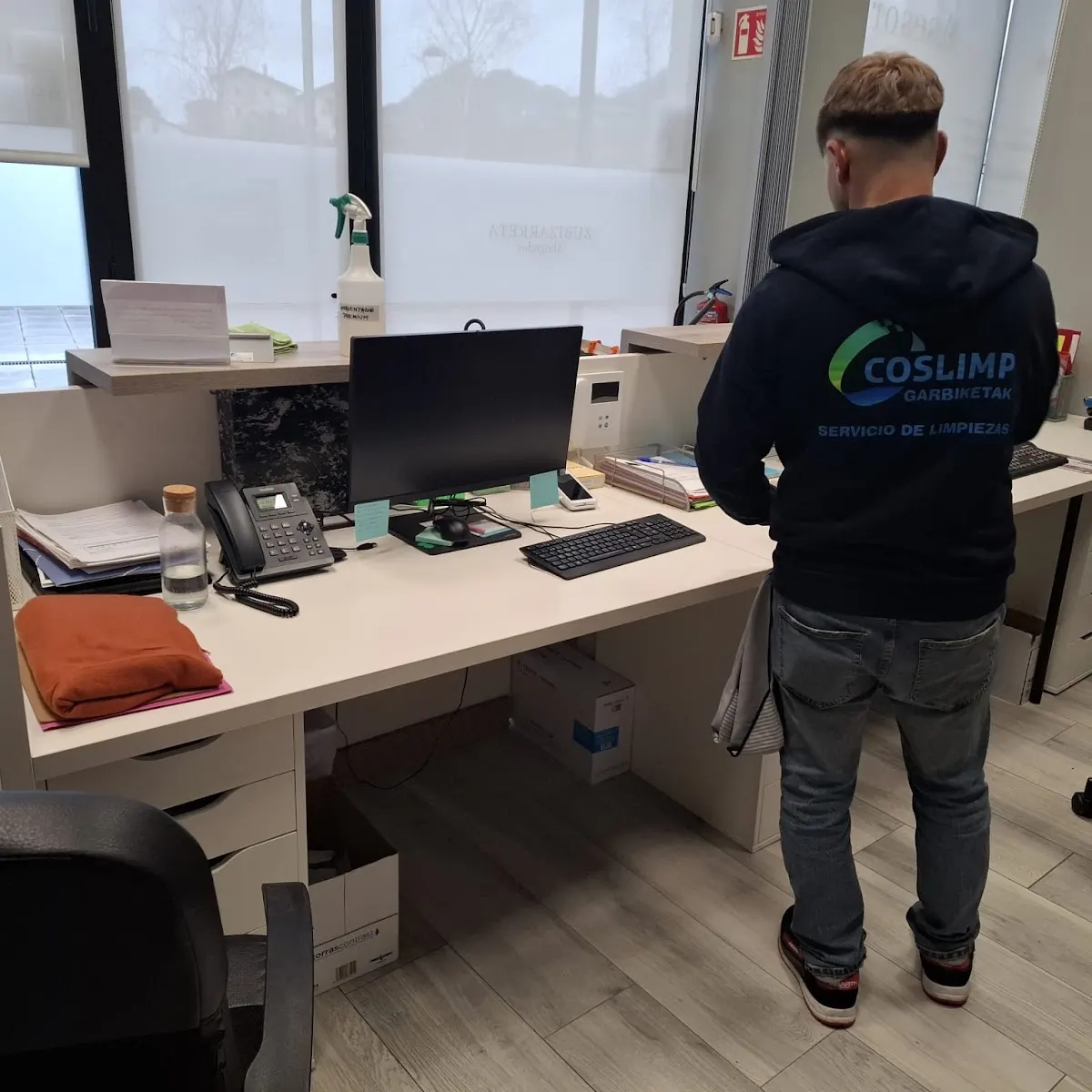 Un trabajador limpia una mesa de oficina; Limpiezas COSLIMP GARBIKETAK.