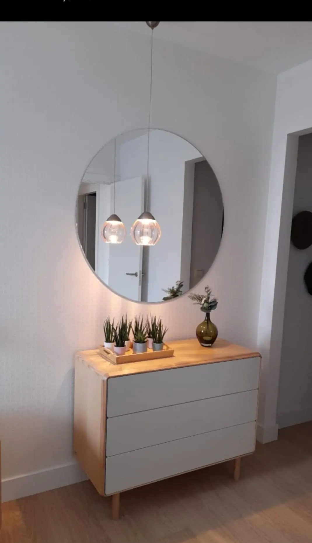 Cómoda de líneas sencillas, espejo redondo y lámparas colgantes en un espacio interior decorado por Loiro.