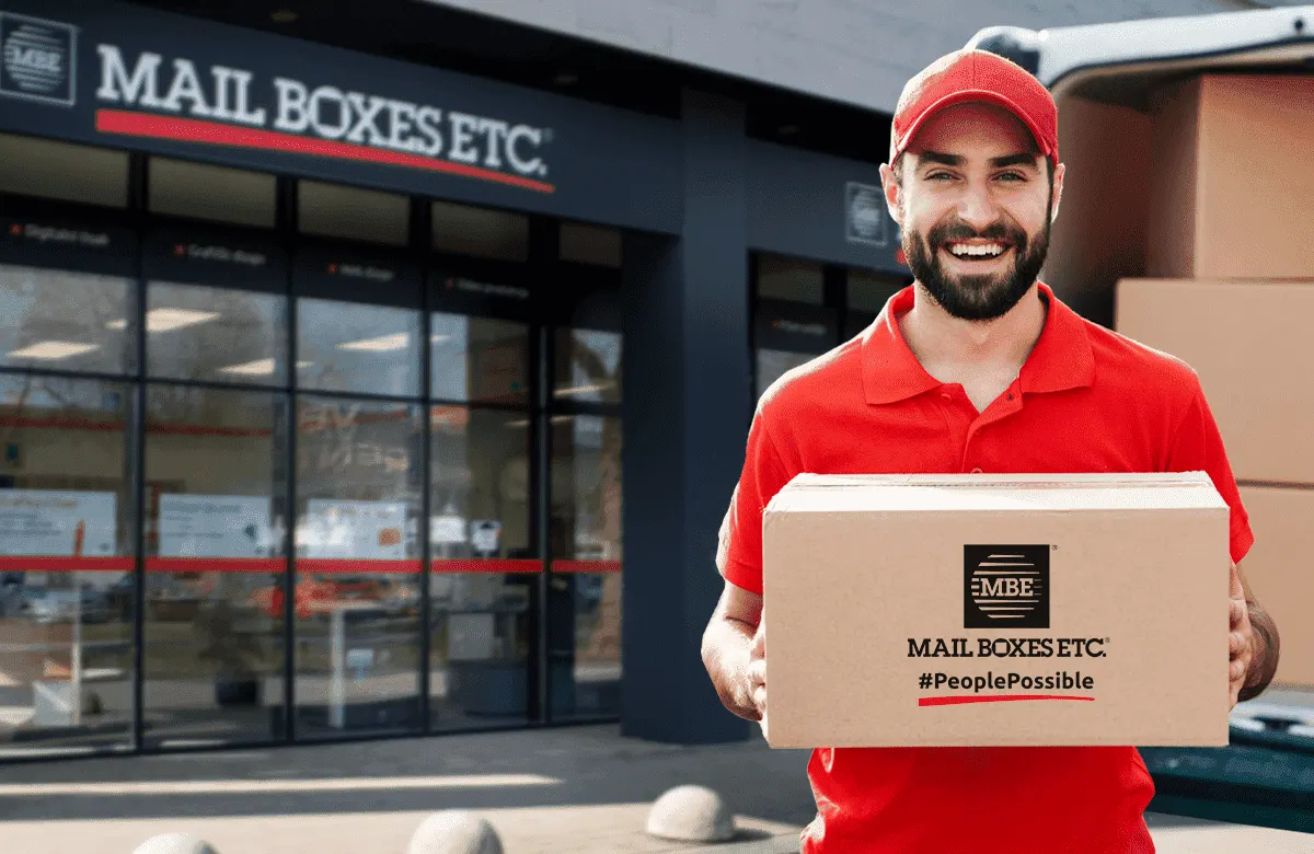 Trabajador de Mail Boxes Etc. con un paquete frente a un local de la cadena